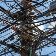 Poste de utilidade urbana com uma rede de fios e cabos entrelaçados contra o céu claro.
