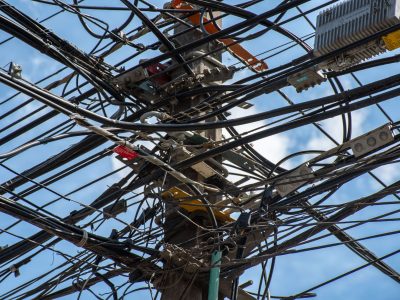 Poste de utilidade urbana com uma rede de fios e cabos entrelaçados contra o céu claro.
