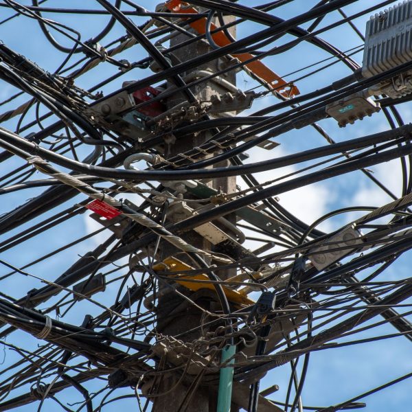 Poste de utilidade urbana com uma rede de fios e cabos entrelaçados contra o céu claro.