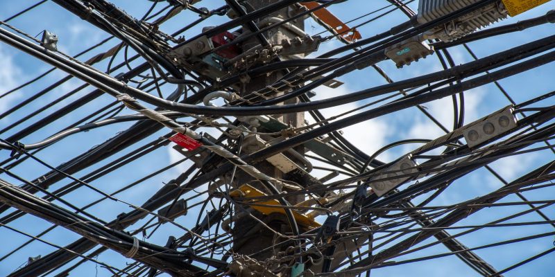 Poste de utilidade urbana com uma rede de fios e cabos entrelaçados contra o céu claro.