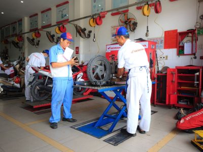 Mecânicos uniformizados trabalham em motocicletas dentro de um centro de serviços da Honda.
