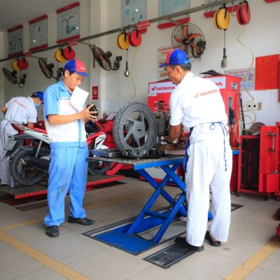 Mecânicos uniformizados trabalham em motocicletas dentro de um centro de serviços da Honda.