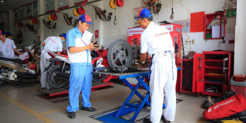 Mecânicos uniformizados trabalham em motocicletas dentro de um centro de serviços da Honda.