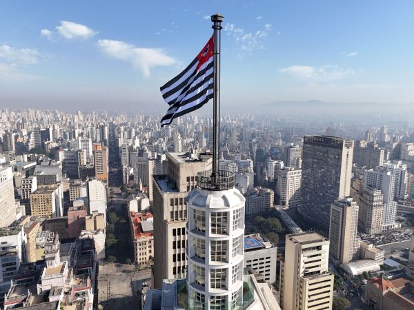 Vista aérea do horizonte de São Paulo com a bandeira do estado em destaque.