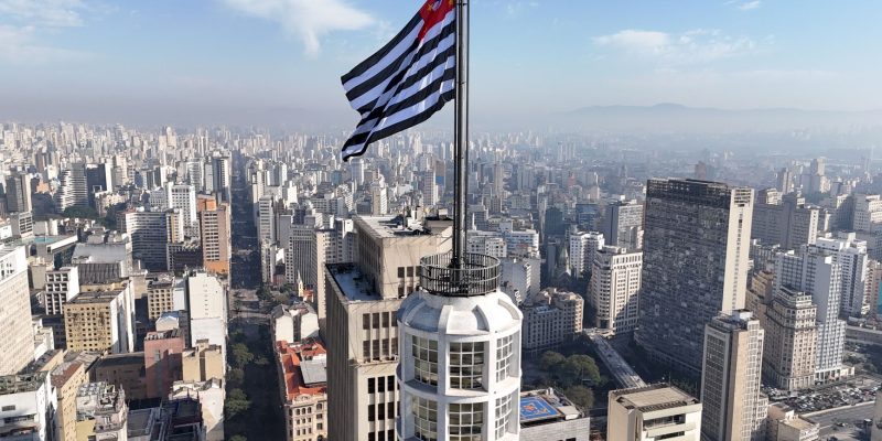 Vista aérea do horizonte de São Paulo com a bandeira do estado em destaque.