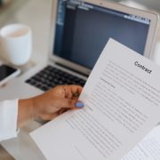 Pessoa segura um documento contratual ao lado de um computador portátil durante uma sessão de trabalho.