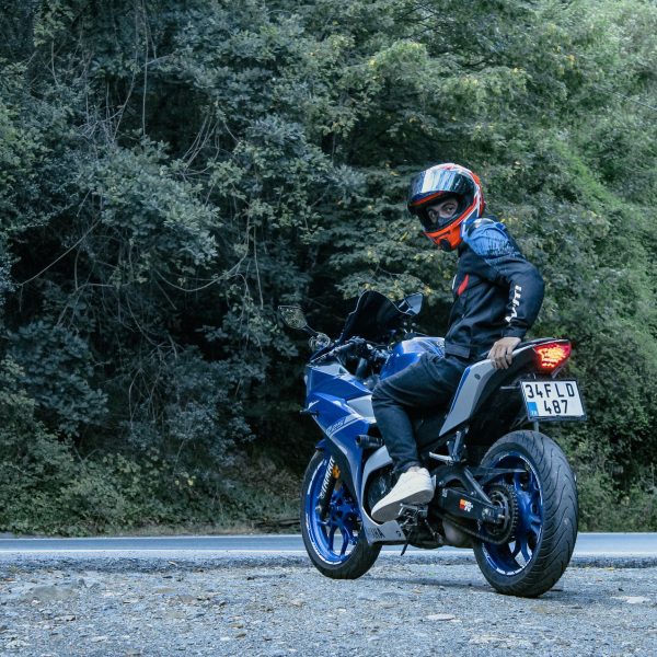 Motociclista usando capacete conduz uma motocicleta Yamaha azul por uma estrada cercada de vegetação.
