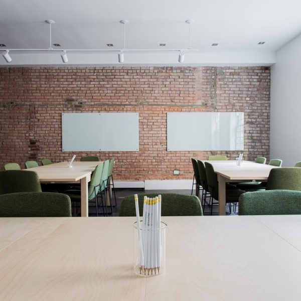 Sala de aula vazia com mesas, cadeiras e paredes de tijolos aparentes.