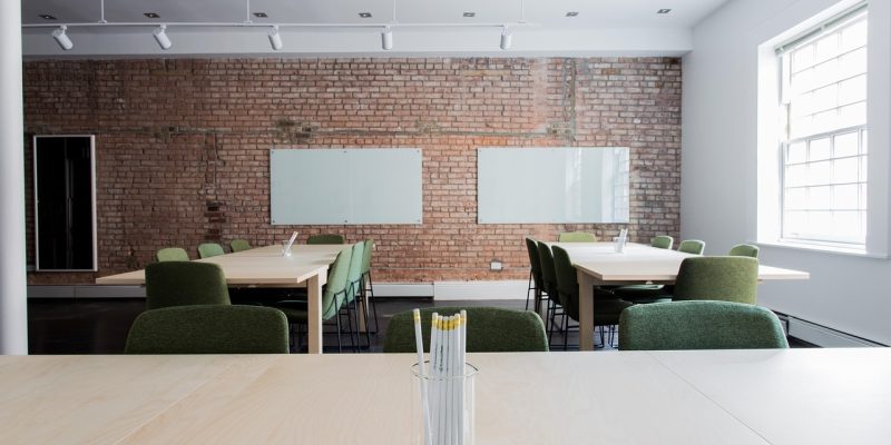 Sala de aula vazia com mesas, cadeiras e paredes de tijolos aparentes.