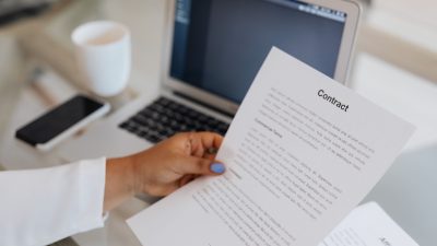 Pessoa segura um documento contratual ao lado de um computador portátil durante uma sessão de trabalho.