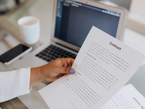 Pessoa segura um documento contratual ao lado de um computador portátil durante uma sessão de trabalho.